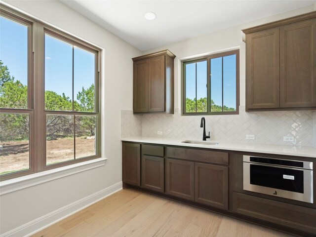 kitchen featuring light wood-type flooring, tasteful backsplash, plenty of natural light, and oven