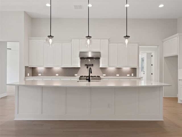 kitchen with a large island with sink, a high ceiling, wall chimney range hood, and white cabinets