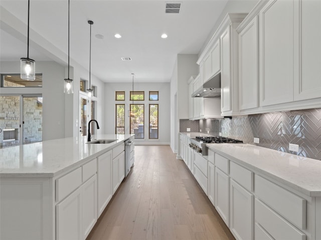 kitchen featuring wall chimney range hood, backsplash, a large island with sink, and appliances with stainless steel finishes