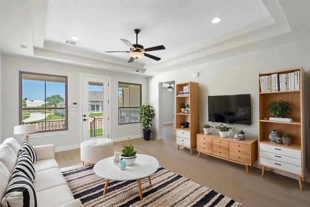 living room featuring ceiling fan, plenty of natural light, light wood-type flooring, and a tray ceiling