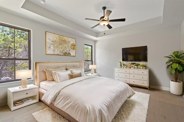 bedroom featuring light hardwood / wood-style floors, ceiling fan, and a tray ceiling