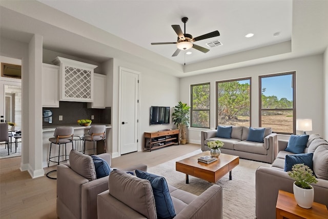 living room featuring ceiling fan, a raised ceiling, and light wood-type flooring