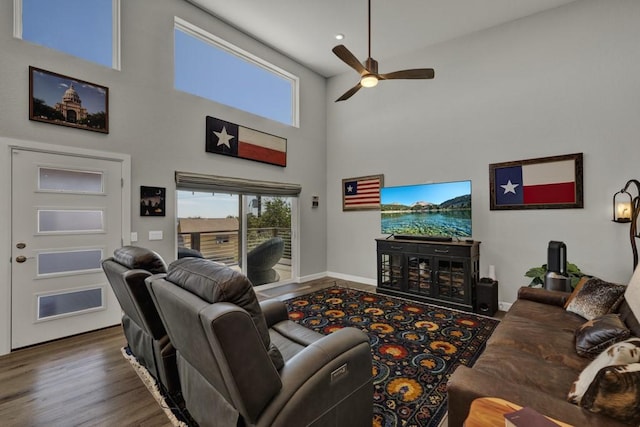 living room with a towering ceiling, baseboards, wood finished floors, and ceiling fan