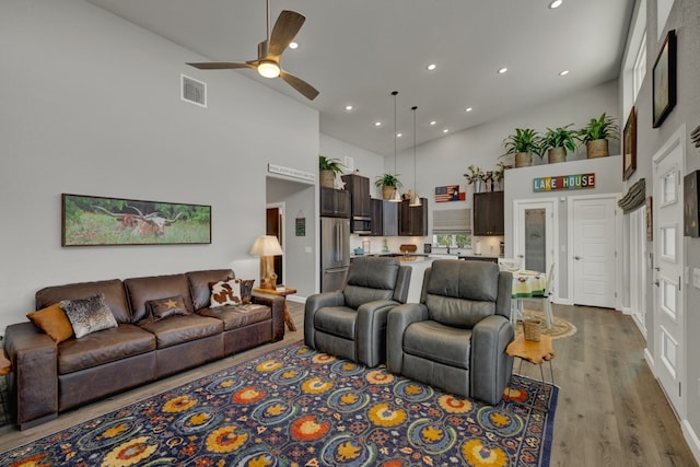 living room with a high ceiling, light wood-type flooring, and ceiling fan