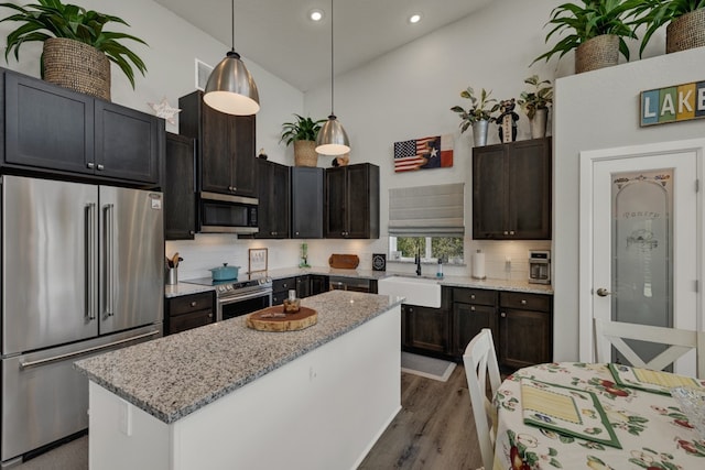 kitchen featuring light stone countertops, stainless steel appliances, sink, a kitchen island, and hanging light fixtures