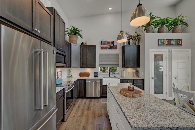 kitchen featuring white cabinets, vaulted ceiling, a kitchen island, appliances with stainless steel finishes, and light hardwood / wood-style floors