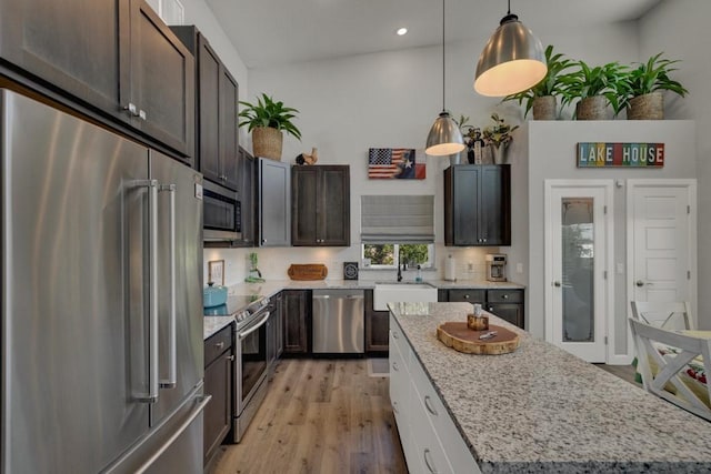 kitchen featuring a sink, appliances with stainless steel finishes, light wood-style floors, light stone countertops, and pendant lighting