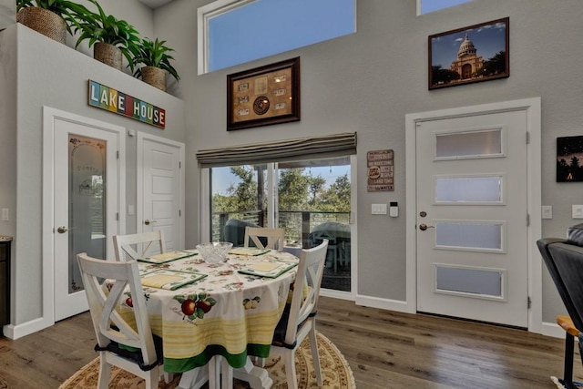dining area with wood finished floors, baseboards, and a towering ceiling