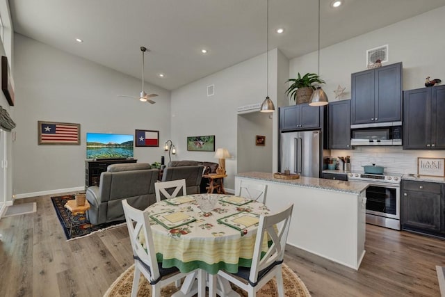 dining room featuring baseboards, visible vents, ceiling fan, high vaulted ceiling, and wood finished floors