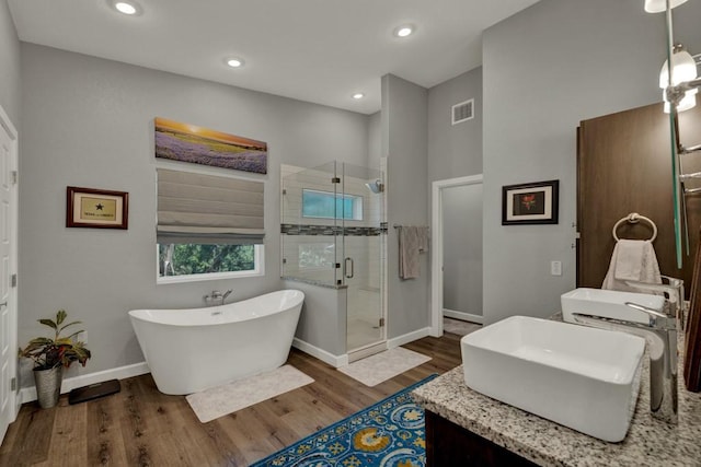 full bathroom featuring vanity, wood finished floors, a freestanding bath, a stall shower, and baseboards