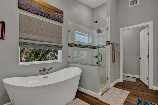 bathroom featuring baseboards, a stall shower, a soaking tub, visible vents, and wood finished floors