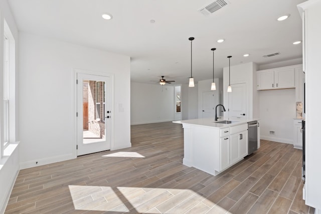 kitchen with white cabinets, decorative light fixtures, a kitchen island with sink, and sink