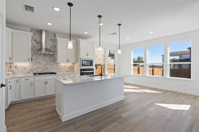 kitchen with white cabinets, oven, wall chimney range hood, and a kitchen island with sink