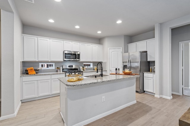 kitchen with appliances with stainless steel finishes, white cabinetry, light wood-type flooring, and sink