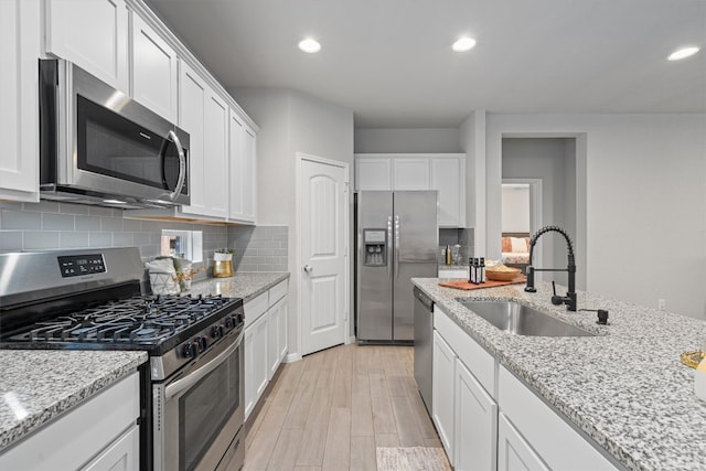 kitchen featuring backsplash, stainless steel appliances, sink, light stone countertops, and white cabinets