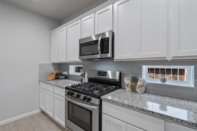 kitchen featuring stainless steel appliances, light hardwood / wood-style floors, decorative backsplash, white cabinetry, and light stone counters