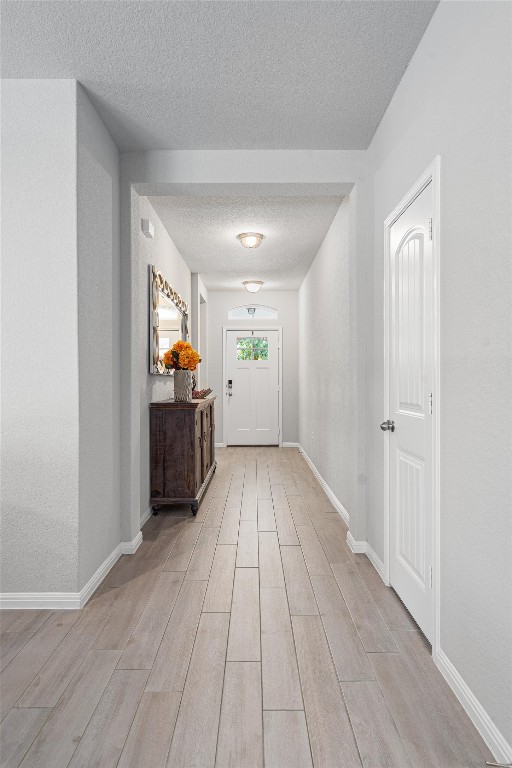 corridor with a textured ceiling and light hardwood / wood-style floors