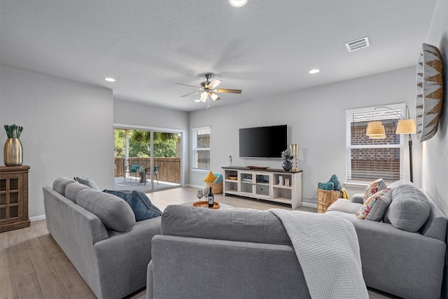 living room featuring ceiling fan, light hardwood / wood-style flooring, and a textured ceiling