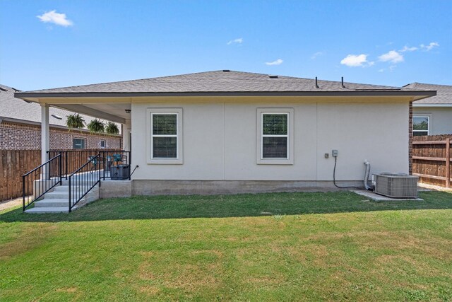 back of house with central AC unit and a yard