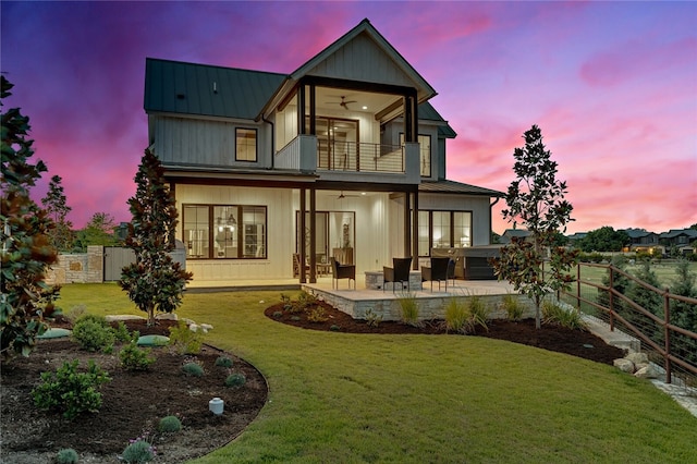 back house at dusk with a patio area, a yard, and a balcony