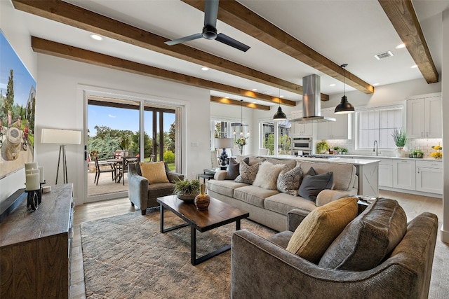 living room with a wealth of natural light, beam ceiling, light hardwood / wood-style floors, and ceiling fan