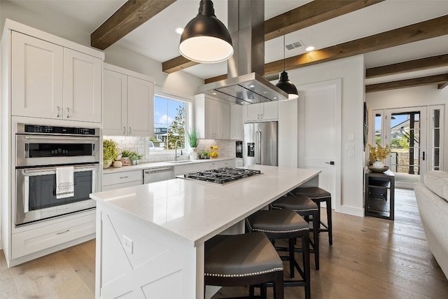 kitchen featuring light wood-type flooring, decorative backsplash, island exhaust hood, appliances with stainless steel finishes, and a wealth of natural light