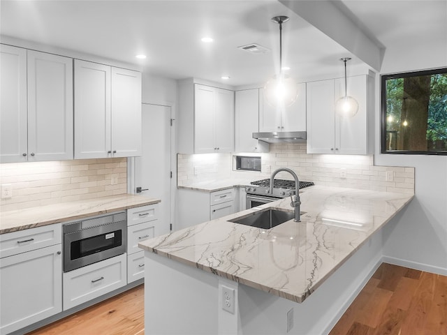 kitchen with light wood-type flooring, backsplash, white cabinets, and decorative light fixtures