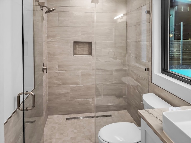 bathroom featuring a shower with door, toilet, vanity, and tile walls