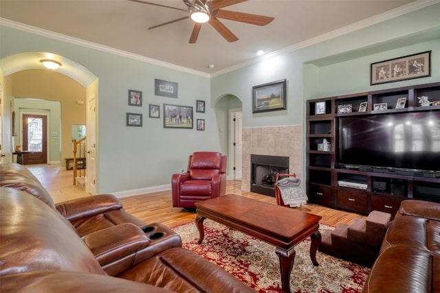 living room with ornamental molding, a tiled fireplace, ceiling fan, and light hardwood / wood-style flooring