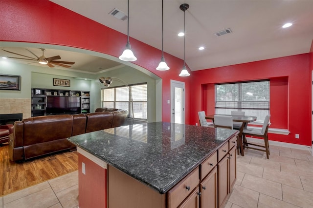 kitchen featuring ceiling fan, light tile patterned flooring, a tile fireplace, hanging light fixtures, and a center island