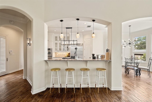 kitchen with dark wood-style floors, crown molding, stainless steel appliances, an inviting chandelier, and glass insert cabinets