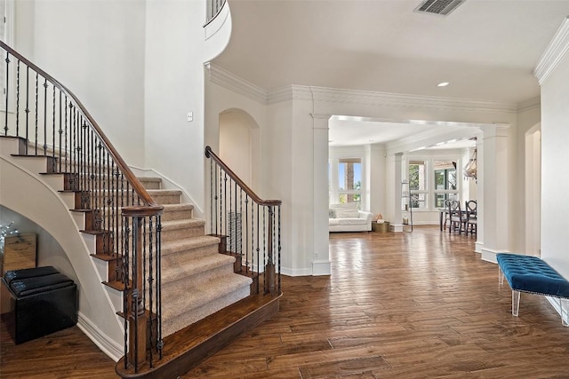 foyer featuring decorative columns, baseboards, visible vents, ornamental molding, and wood finished floors