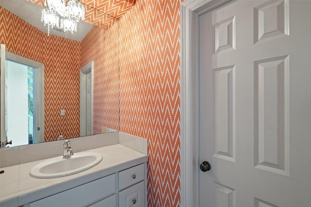 bathroom with vanity, an inviting chandelier, and wallpapered walls