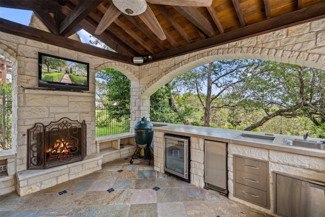 view of patio with exterior kitchen, wine cooler, an outdoor stone fireplace, and a sink