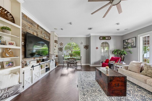 living room featuring dark hardwood / wood-style flooring, built in shelves, crown molding, and ceiling fan