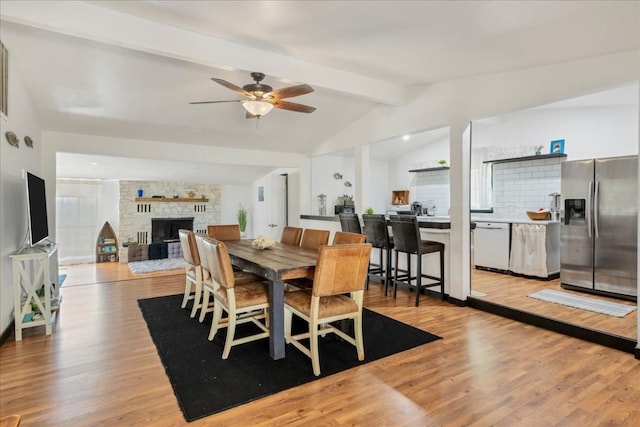 dining room with ceiling fan, a large fireplace, lofted ceiling with beams, and light hardwood / wood-style flooring