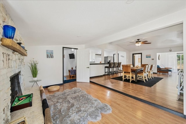 living room featuring light hardwood / wood-style floors, lofted ceiling with beams, ceiling fan, and a fireplace