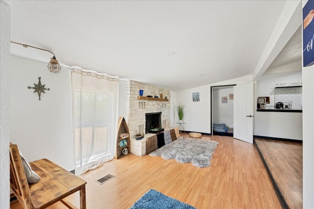 living room featuring a fireplace, lofted ceiling, light wood-type flooring, and brick wall