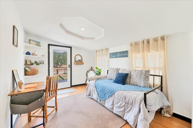 bedroom featuring a raised ceiling, light hardwood / wood-style flooring, and access to exterior