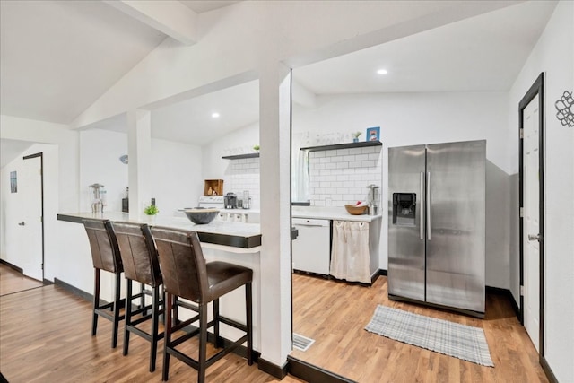 kitchen with stainless steel fridge, vaulted ceiling with beams, light hardwood / wood-style flooring, and tasteful backsplash