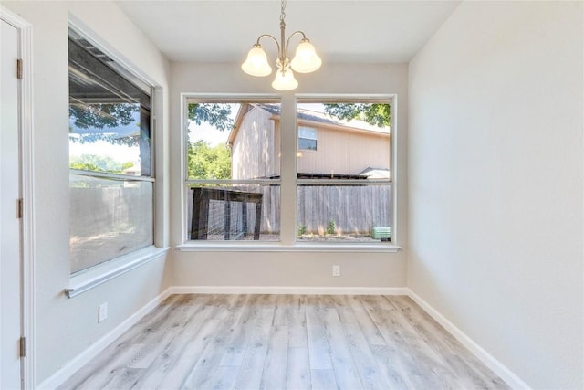 unfurnished dining area featuring baseboards, a notable chandelier, and light wood finished floors