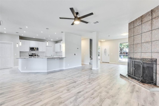 unfurnished living room with a fireplace, light wood finished floors, visible vents, stairway, and baseboards