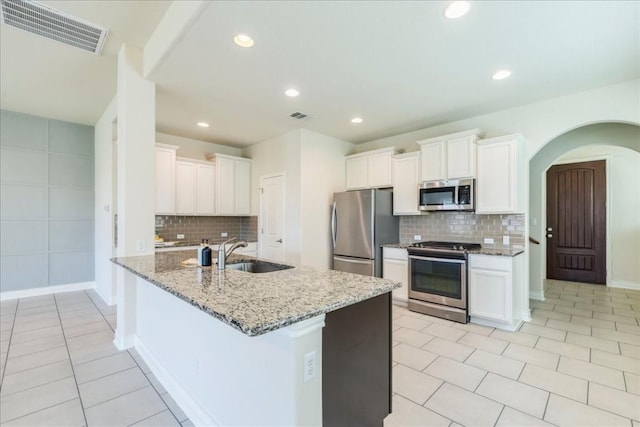 kitchen with light stone counters, arched walkways, stainless steel appliances, visible vents, and a sink