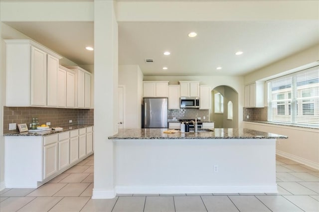 kitchen with arched walkways, a sink, white cabinets, appliances with stainless steel finishes, and dark stone countertops