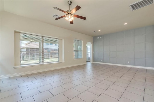 empty room with arched walkways, ceiling fan, visible vents, and baseboards