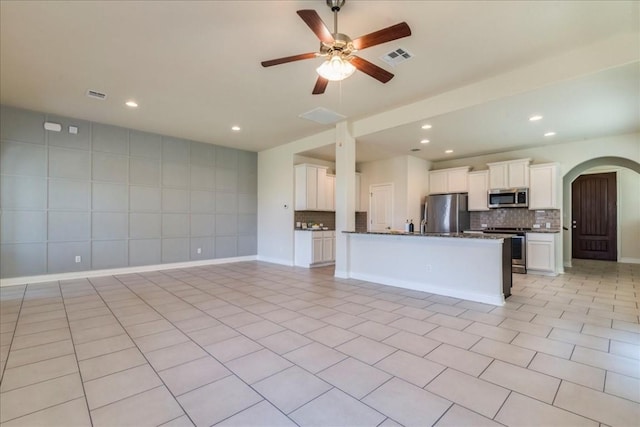 kitchen with arched walkways, backsplash, appliances with stainless steel finishes, open floor plan, and white cabinetry