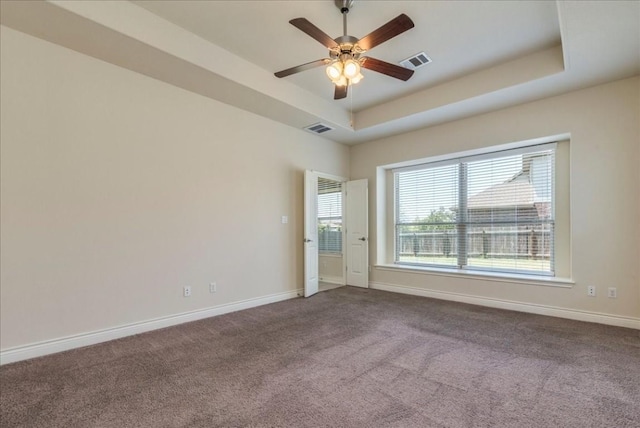 carpeted empty room with a ceiling fan, a tray ceiling, visible vents, and baseboards