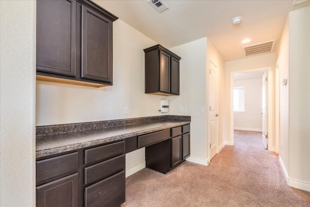 interior space with built in desk, dark countertops, visible vents, and dark brown cabinetry