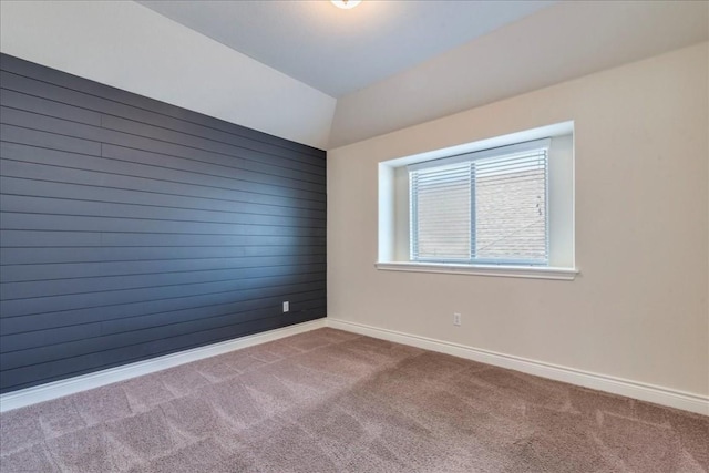 empty room featuring lofted ceiling, wood walls, baseboards, and carpet flooring