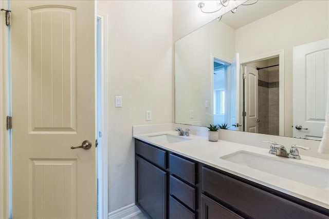 full bathroom featuring tiled shower, a sink, baseboards, and double vanity